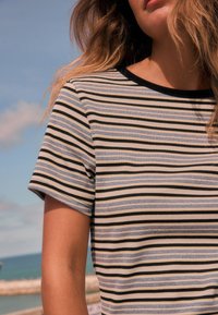 Camiseta de rayas con mangas cortas, que presenta líneas horizontales en tonos azul y negro sobre un fondo claro, textura acanalada y cuello oscuro.