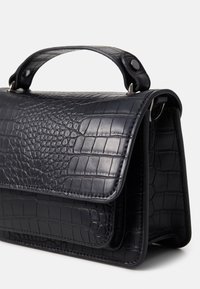 Sac à main en cuir noir embossé crocodile avec une forme structurée, une poignée supérieure et une fermeture magnétique. Présente des coutures visibles et des accessoires métalliques.