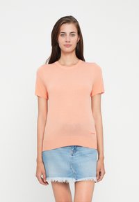 Breskev kratkoslečen pleten sweatshirt z okroglim izrezom in ravnim robom, združen z lahkim modrim denim mini krilom z raztrganimi robovi.