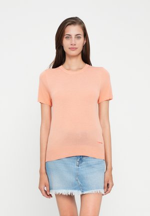 Maglione a maniche corte in pesco con scollatura rotonda e orlo dritto, abbinato a una mini gonna in denim azzurro chiaro con bordi sfrangiati.