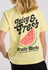 T-shirt giallo in cotone con una grande grafica di anguria e testo nero che recita "Mercato di Frutta Succosa e Fresca Prodotto di Qualità 100% Organico."