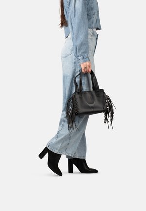 Borsa in pelle nera con accenti di frange, manici intrecciati e logo impresso. Abbinata a una giacca di jeans azzurro chiaro e jeans a gamba larga.