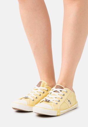 Yellow canvas sneakers with white laces, rubber toe caps, and a brown logo patch. Features a low-profile design and textured fabric.