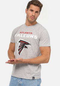 Šedé bavlněné tričko s nápisem "Atlanta Falcons" v červené a bílé barvě, s logem sokola v černé a červené. Kulatý výstřih a krátké rukávy.