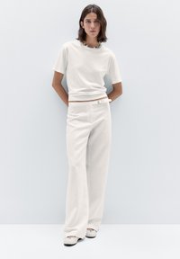 Witte t-shirt met korte mouwen en een gestructureerde kraag, gecombineerd met hoge, wijde witte pantalon. Outfit compleet gemaakt met lichtgrijze schoenen.