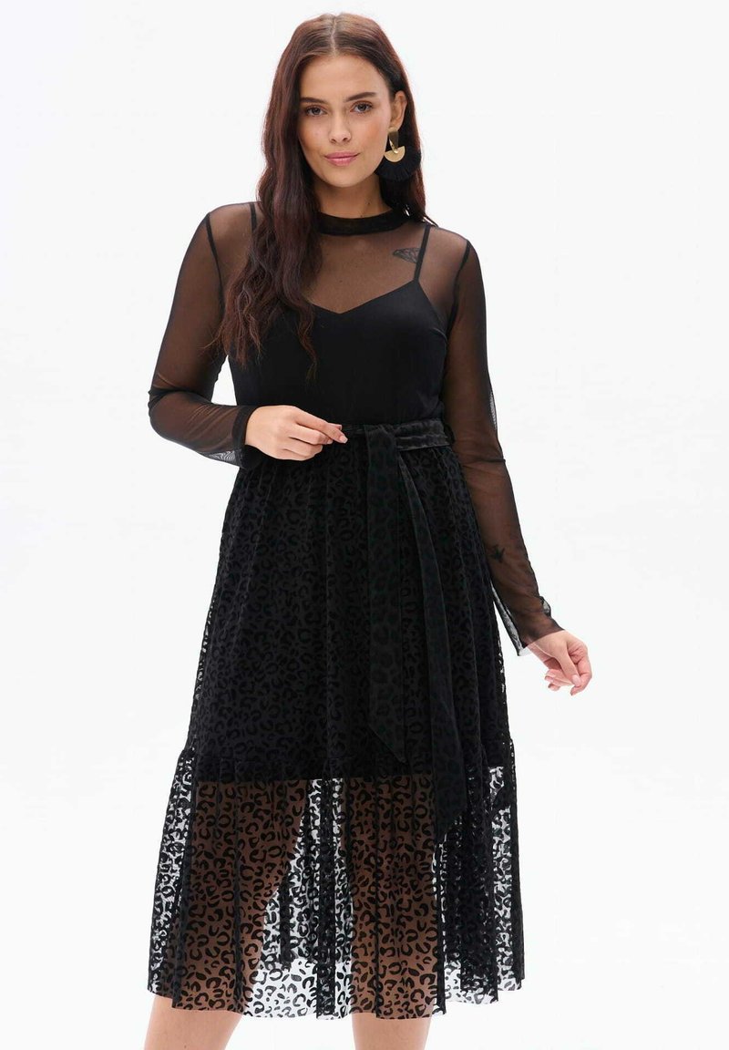 Czarna sukienka z dopasowanym topem, przezroczystymi długimi rękawami i zwiewną spódnicą w leoparda. Posiada wiązany detal w talii.