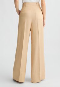 Pantaloni beige a gamba larga realizzati in tessuto morbido, con vita alta, tasca posteriore e una vestibilità rilassata che scivola elegantemente.