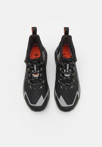 Czarno-szare buty sportowe z siateczkową cholewką, zygzakowatym wzorem po bokach, kontrastującą pomarańczową wkładką i sznurówkami zapewniającymi pewne dopasowanie.
