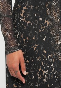 Langärmliges Kleid im Schlangenprint in Schwarz-, Beige- und Brauntönen. Aus einem strukturierten, dehnbaren Stoff mit komplizierten Mustern.