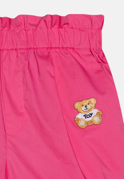 Shorts pour enfants rose avec une taille élastique et un patch brodé représentant un ours en peluche avec l'inscription "JOUET". Tissu doux et lisse avec des poches latérales.