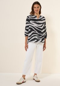 Sort og hvid zebra-stribet bluse med trekvartærmer, V-hals og afslappet pasform, parret med hvide brede bukser og afslappede sneakers.