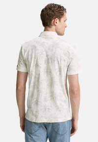 Camisa polo de manga corta, color beige claro con un sutil patrón de hojas de palma, tejido texturizado, cuello acanalado y corte estándar.