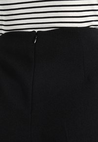 Černá sukně s vysokým pasem a viditelným zipem na zadní straně, spojená s černobílým topem s vodorovnými pruhy.