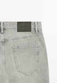 Lichtgrijze denim jeans met achterzak en zwart "Massimo Dutti" merklabel op de tailleband tegen een witte achtergrond.