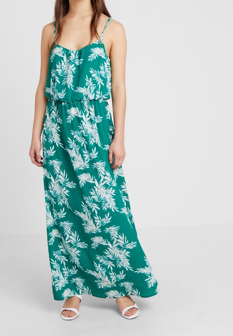 Grön maxiklänning med vitt palmbladsmönster, lättviktsmaterial, avslappnad passform, justerbara spaghetti-axelremmar och cinchad midja.