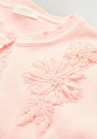 Rosa stickad tröja med blommig broderi. Har texturerad tyg, volangkrage och pärlprydnader runt tre tygblommor.