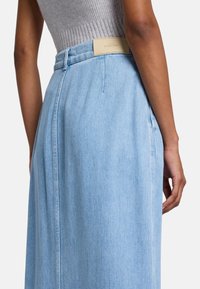 Lichtblauwe denim rok met een aansluitende taille, een achterkant met een rechthoekig label en subtiele plooien langs de zijkanten.