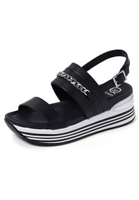 Sandali neri con una suola spessa, dotati di due cinture larghe, un accento a catena e una suola a righe. La parte superiore presenta una texture in pelle liscia.