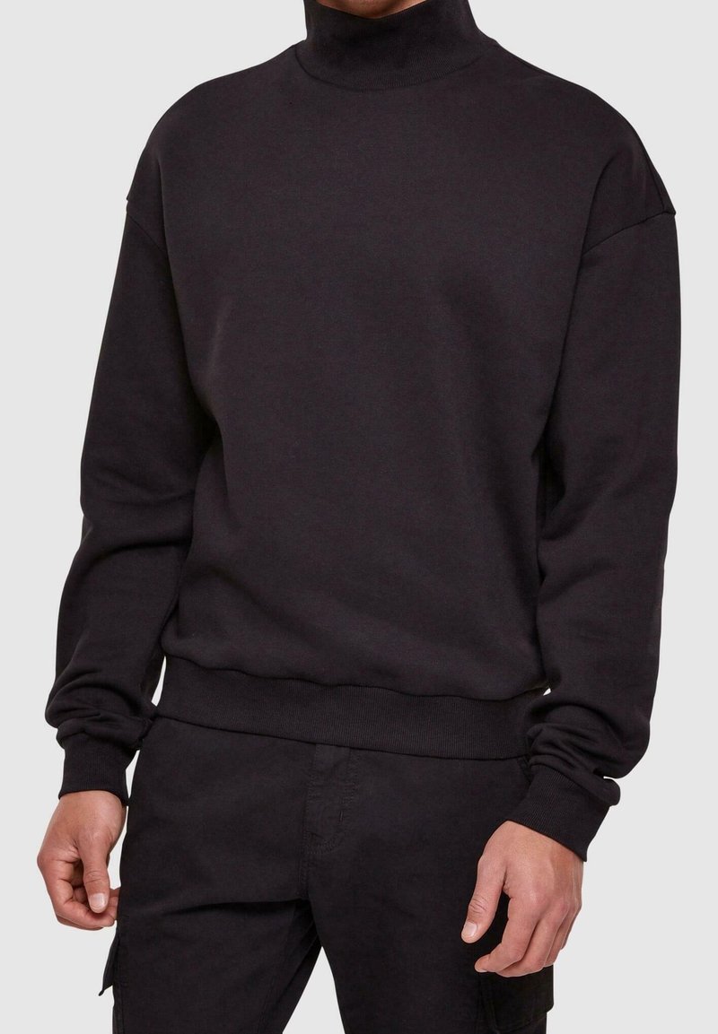 Sweat-shirt col roulé noir en tissu doux, avec épaules tombantes et poignets et ourlet côtelés pour une coupe décontractée.