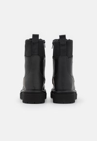 Botas negras hasta el tobillo con un acabado de cuero suave, una suela de goma resistente y un zipper lateral. Presentan una sección superior de tela para añadir textura.