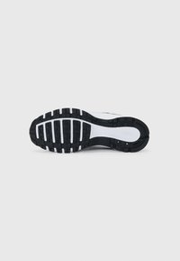 Sole di scarpa da corsa in bianco e nero con un motivo testurizzato, caratterizzata da scanalature profonde per la trazione e un'area della punta rinforzata.