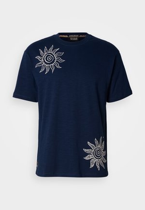 Maglietta di cotone blu navy con ricamo bianco a motivo raggiante sul petto a sinistra e nell'angolo inferiore destro. Scollo rotondo, maniche corte.