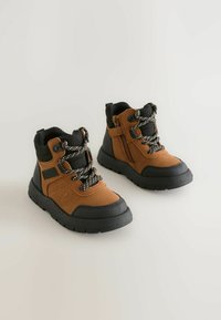 Ruske trekking kengät mustilla kumipohjilla, joissa on teksturoitu päällinen, ruudulliset nauhat ja sivumallinen vetoketju, joka helpottaa pukemista.