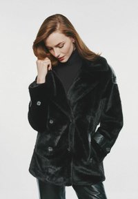 Czarny sztuczny futrzany płaszcz z podwójnym zapięciem, dużymi guzikami oraz skórzanymi akcentami na ramionach i mankietach. Gładka textura.