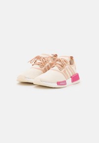 Ljusrosa och krämfärgade sneakers med en strukturerad tygöverdel, snörning och en framträdande rosa Adidas-logotyp på sidan. Har gummisulor.