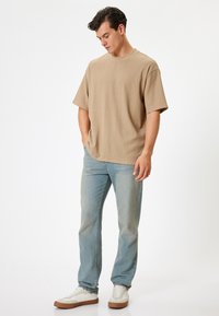 Beige tekstureret T-shirt med korte ærmer parret med lyseblå jeans og hvide sneakers med brune detaljer. Enkel, afslappet stil.