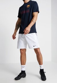 Navy cotton T-shirt with Barcelona logo and red print, paired with white Nike shorts, black soccer shoes, and white socks with black accents.