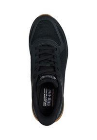 Chaussure de sport noire à enfiler avec un upper en maille, un col rembourré et une semelle en caoutchouc. Présente un logo sur la semelle intérieure et des accents texturés sur les côtés.
