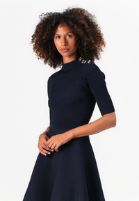 Top navy a costine con maniche corte, scollatura alta e dettagli decorativi in oro sulle spalle, abbinato a una gonna a campana coordinata.