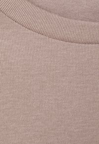 Beige ribbat tyg i närbild, med en rund halsringning och en slät yta samt jämn sömnad. Stickningen är lätt och anpassningsbar.