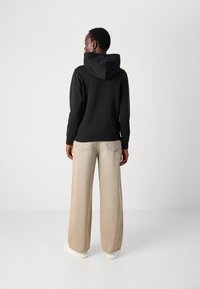 Sudadera negra con capucha ajustable, combinada con pantalones de pierna ancha en beige claro y zapatillas blancas, mostrando un ajuste relajado y un diseño minimalista.