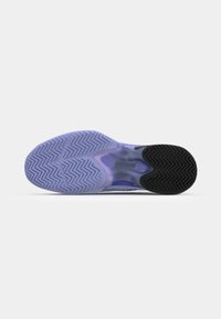 Semelle de chaussure avec un motif texturé en zigzag. Matériau en caoutchouc violet avec une section de talon noire. Nom de la marque "Lacoste" visible sur la semelle.