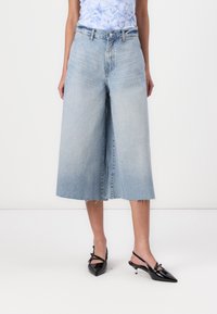 Jasnoniebieskie dżinsowe kuloty z wysokim stanem, z surowym wykończeniem i bocznymi kieszeniami, zestawione z czarnymi lakierowanymi sandałami na obcasie.