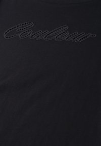 Tissu noir avec texte en script brodé en relief "coutour" en fil foncé près du centre supérieur.
