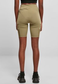 Shorts de vélo vert olive avec une taille haute, une texture lisse et des poches latérales. Portés avec des bottines noires à surface texturée.