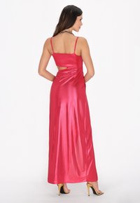 Abito maxi in satin fucsia con spalline sottili, dettaglio sul retro aperto e silhouette fluida. Presenta una texture liscia e lucida e una drappeggiatura sottile.