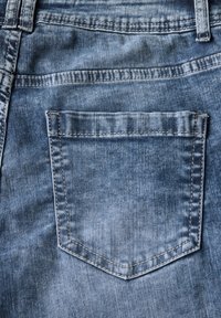 Gros plan sur un tissu en denim bleu clair présentant une poche arrière rectangulaire, avec des détails de couture et de texture visibles.