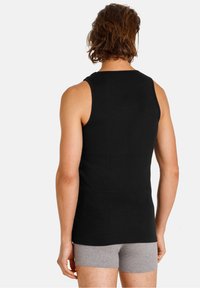 Canotta nera senza maniche in tessuto a coste, design aderente, vista posteriore. Indossata con pantaloni boxer grigi.