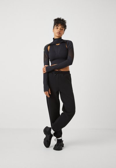 Fekete, hosszú ujjú, crop top hálós részletekkel, laza fekete nadrággal és fekete sportcipővel párosítva. Az öltözet állványnyakkal rendelkezik.