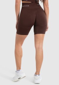 Gli shorts da bicicletta marroni presentano un'alta vita con dettagli del logo in bianco. Il tessuto ha una trama liscia, offrendo una silhouette aderente.