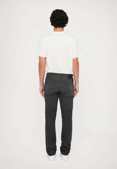 Jeans de ganga pretos com um design de perna reta, apresentando bolsos traseiros com detalhes em costura, usados com uma t-shirt branca simples.