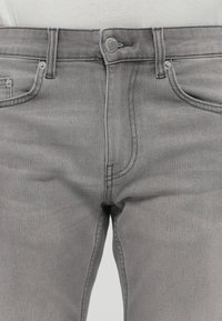 Jeans in denim grigio con un taglio classico, tasche frontali e chiusura con zip e bottone. Texture liscia e dettagli di cucitura sottili.