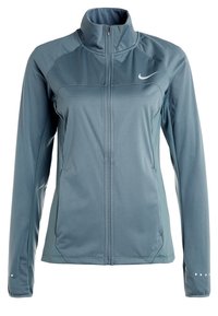 Veste Nike bleu clair à fermeture éclair intégrale avec col haut, manches longues, poches latérales et points réfléchissants près des poignets.