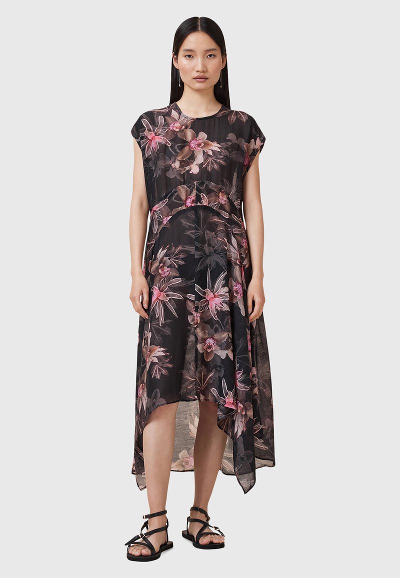 Abito nero floreale con maniche corte, tessuto trasparente, orlo asimmetrico, caratterizzato da motivi floreali rosa e beige. Abbinato a semplici sandali neri.