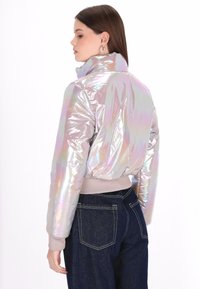 Irydescencyjna kurtka bomberka z wysokim kołnierzem, o jedwabistej teksturze i elastycznym pasie. Połączona z ciemnym dżinsami, prezentująca swobodny wygląd.