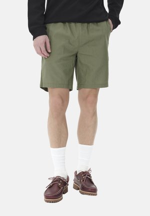 Pantalones cortos verde caqui con un corte holgado y cinturilla elástica, combinados con calcetines blancos y zapatos náuticos marrones.